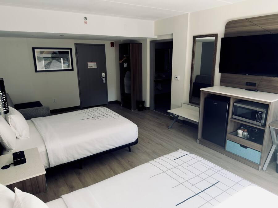 Ein Hotelzimmer mit Bett, Nachttisch, Fernseher, Kleiderschrank und einer kleinen Küchenzeile.