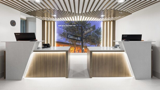 A modern reception desk with two computer stations, a clock, and a large digital display with street signs. - La Quinta Inn & Suites by Wyndham Atlanta Roswell (Roswell)