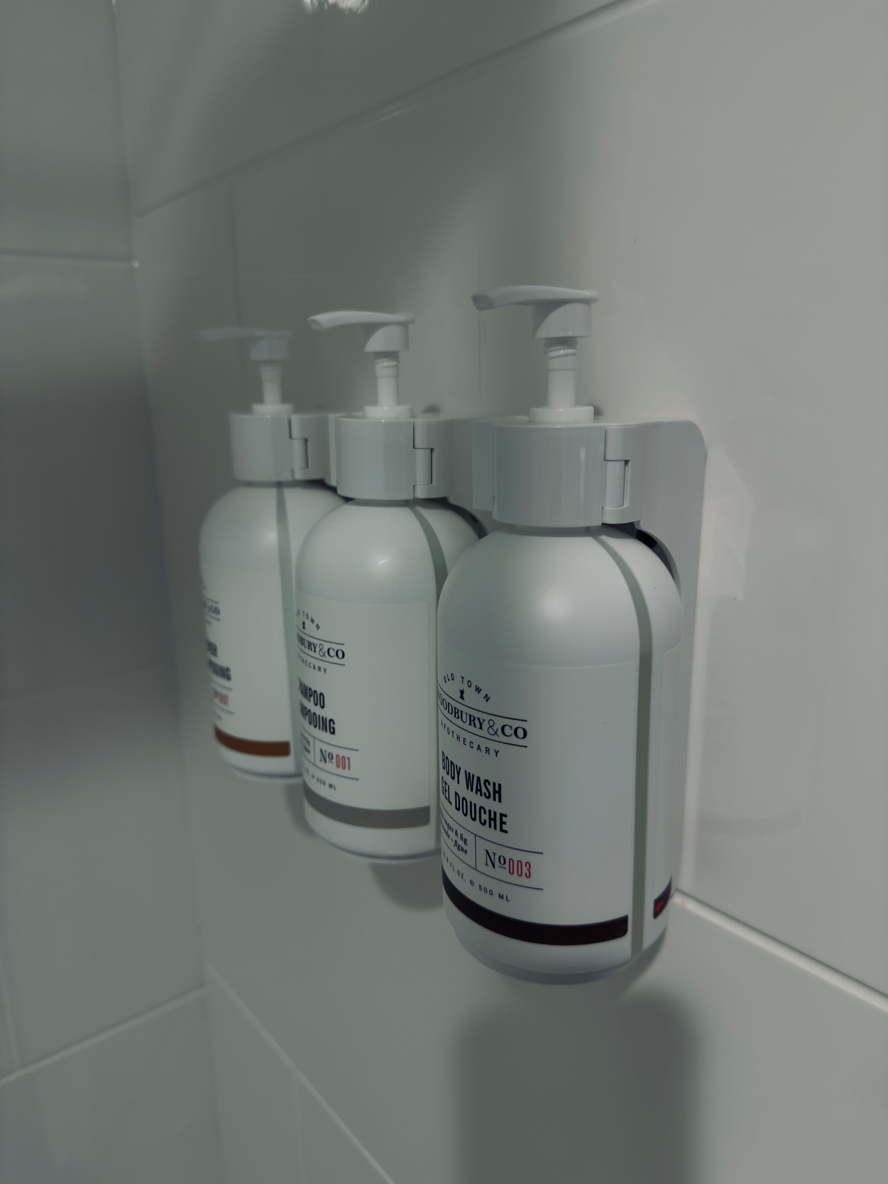 Three bottles of Old Town Body Wash Gel Douche on a white tiled wall.