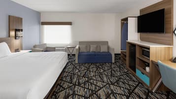 A hotel room with a large bed, a sofa, a desk with a flat-screen TV, and a wardrobe.