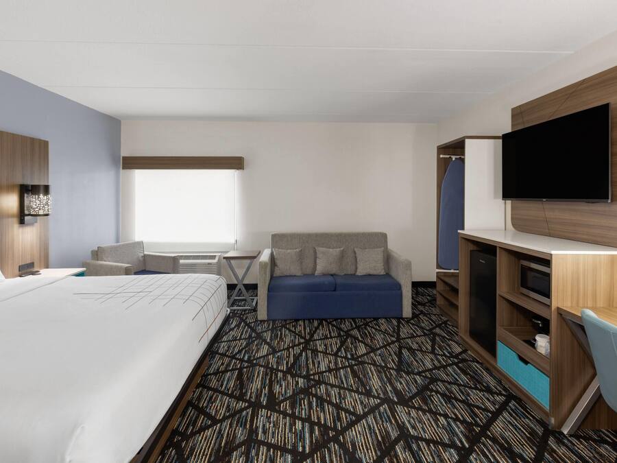A hotel room with a large bed, a sofa, a desk with a flat-screen TV, and a wardrobe.