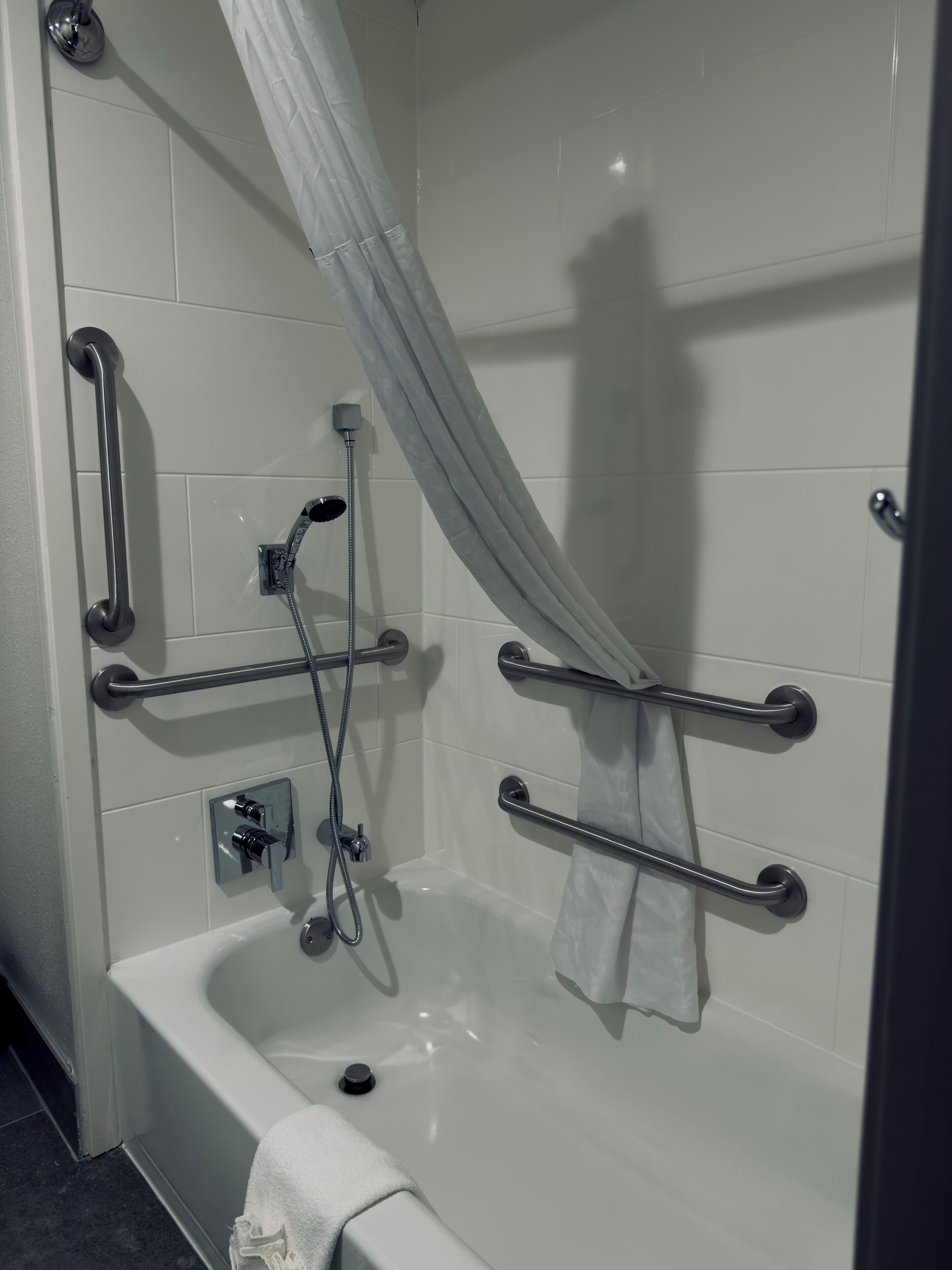 Un baño moderno con bañera, barras de apoyo, ducha y cortina.