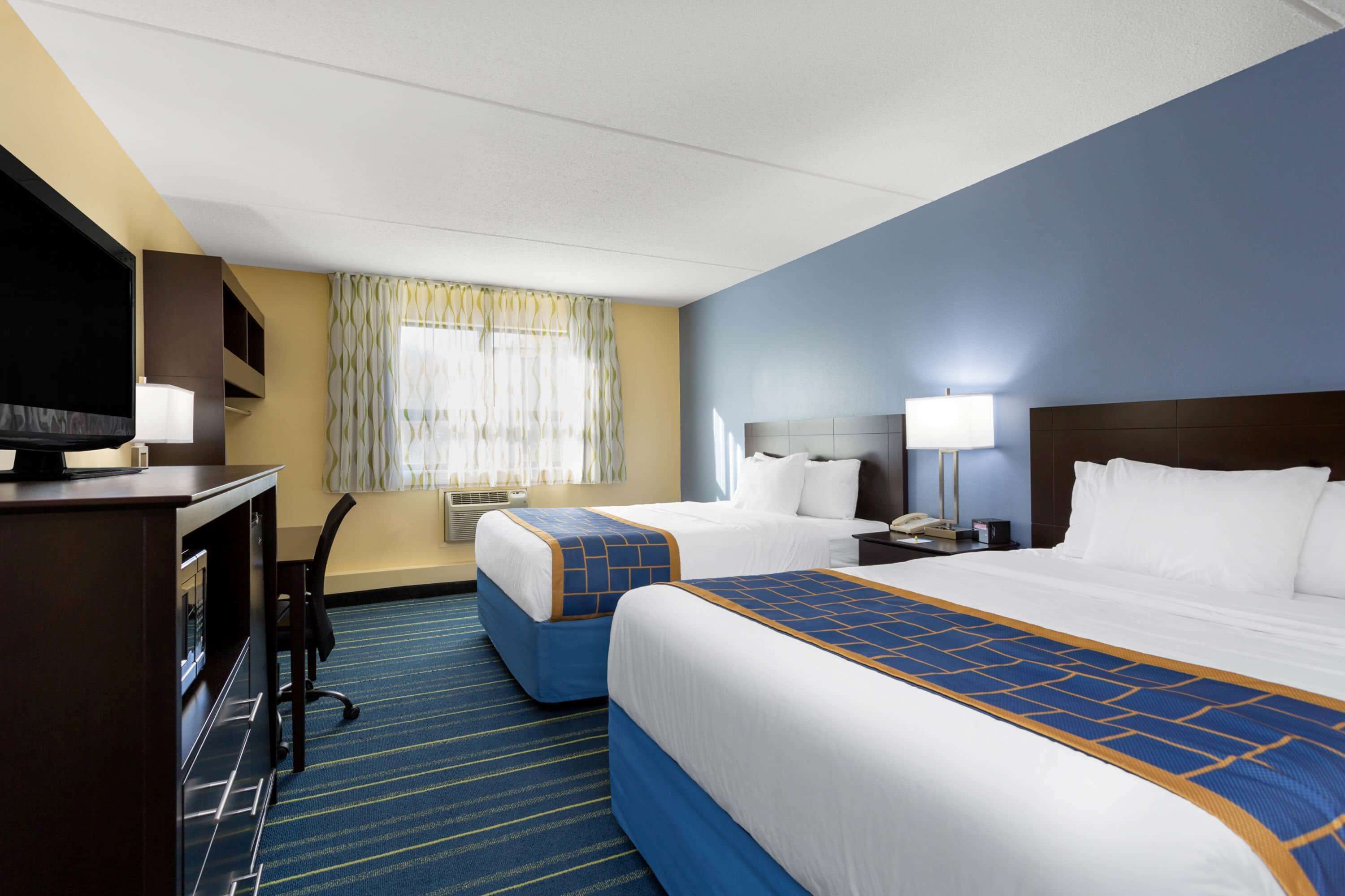 A hotel room with two beds, a desk with a television, and a window with curtains.