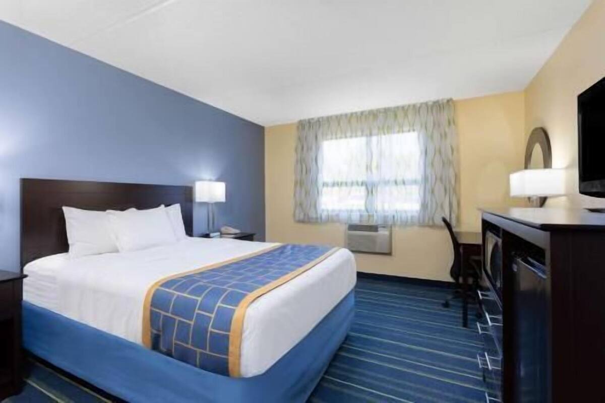 A hotel room with a bed, a desk, a chair, a television, and a window with curtains.