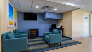 A hotel lobby with teal armchairs, a flat-screen TV, a fireplace, and a door marked with a wheelchair symbol.