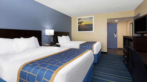 A hotel room with two beds, a desk, a TV, and a painting on the wall.