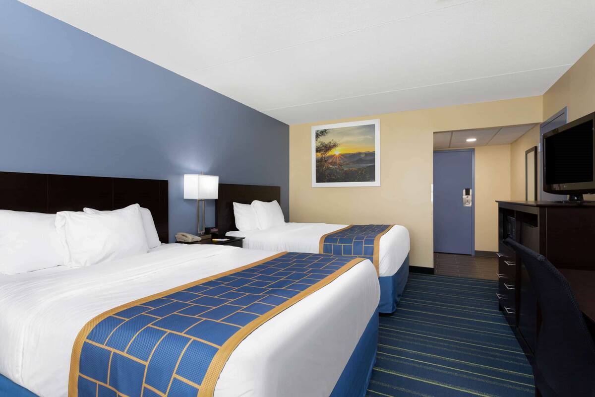 A hotel room with two beds, a desk, a TV, and a painting on the wall.