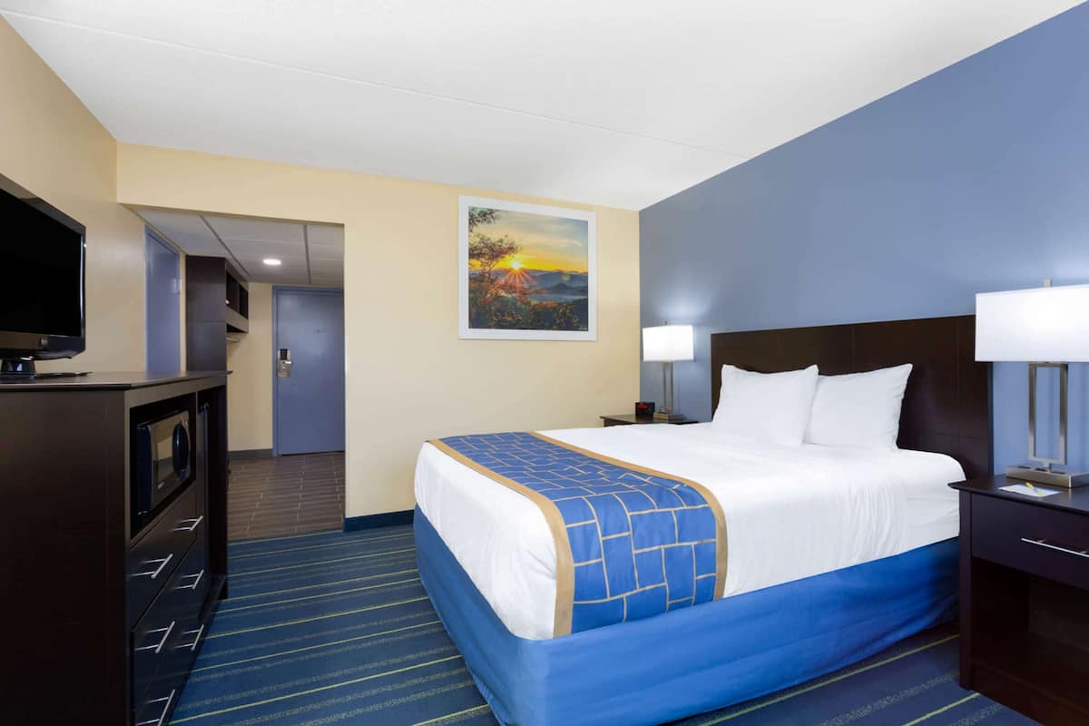 A hotel room with a bed, a desk, a television, a painting, and a lamp.