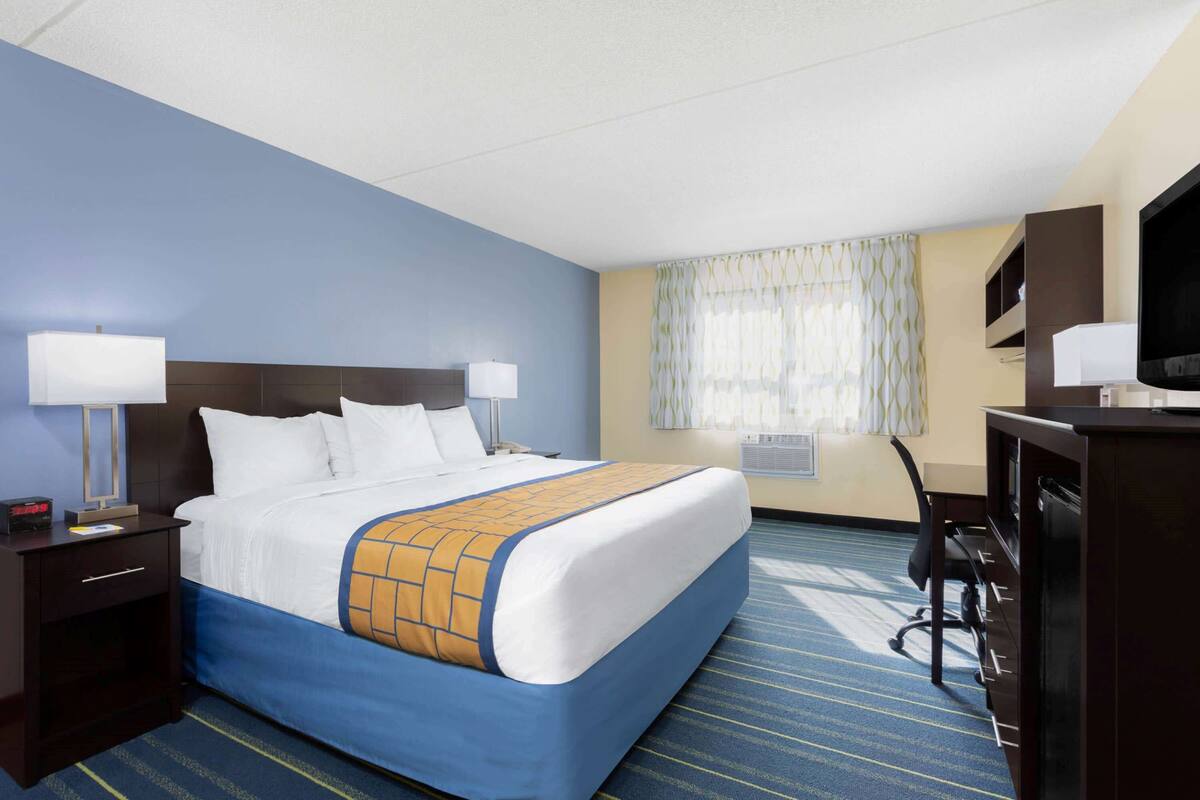 A hotel room with a large bed, two bedside tables with lamps, a desk with a chair, a television, and a window with curtains.