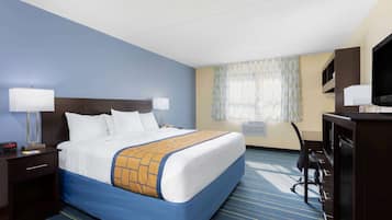 Habitación de hotel con una cama grande, dos mesitas de noche con lámparas, un escritorio con silla, un televisor y una ventana con cortinas.
