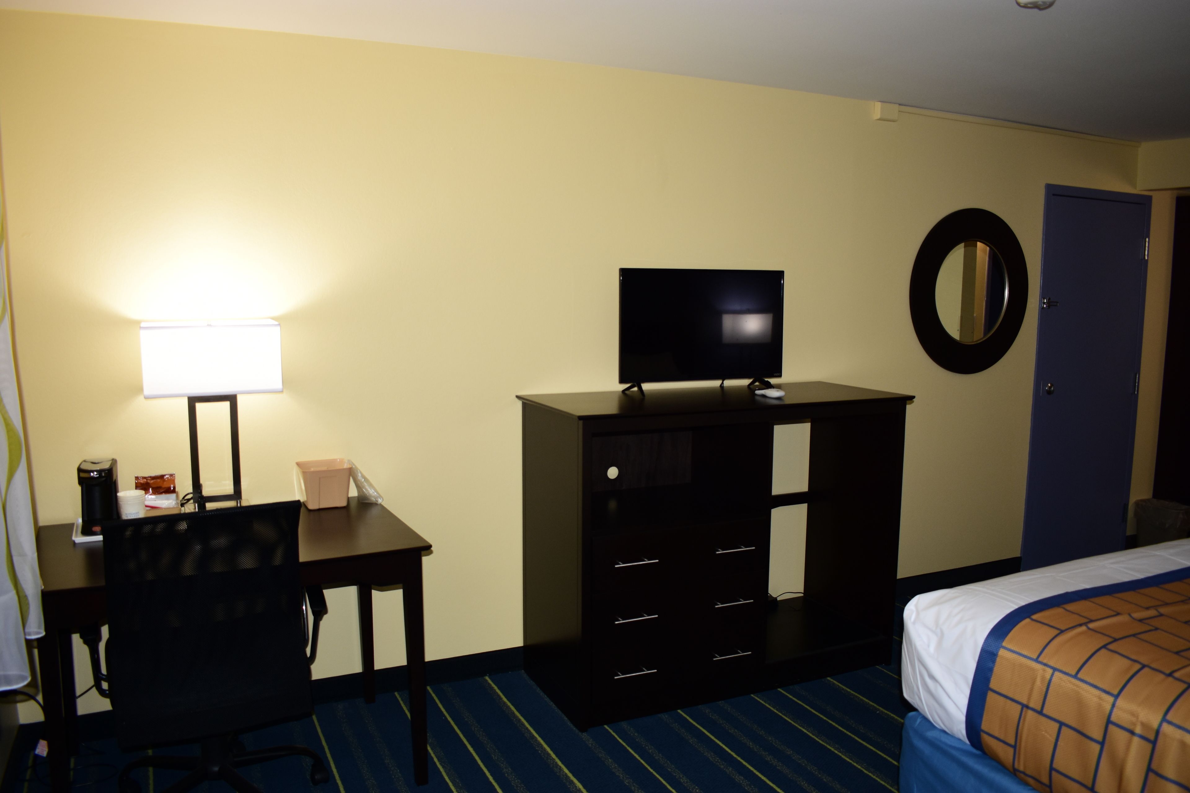 Une chambre d’hôtel équipée d’un bureau, d’une chaise, d’une télévision, d’une commode, d’un lit et d’une porte.