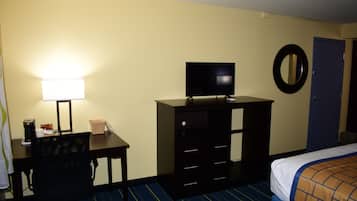 Une chambre d’hôtel équipée d’un bureau, d’une chaise, d’une télévision, d’une commode, d’un lit et d’une porte.