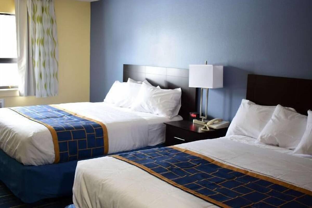 Two beds with white linens and blue headboards, a bedside lamp, and a telephone on a nightstand.