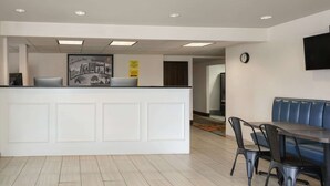 A reception area with a white counter, a framed cityscape picture, and a clock on the wall. - Super 8 by Wyndham Portland ME (Westbrook)