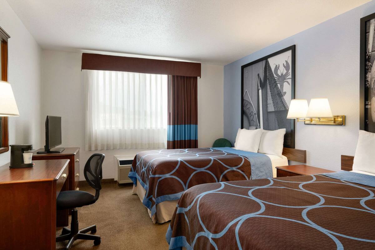 A hotel room with two beds, a desk, a chair, a TV, and a window with curtains.