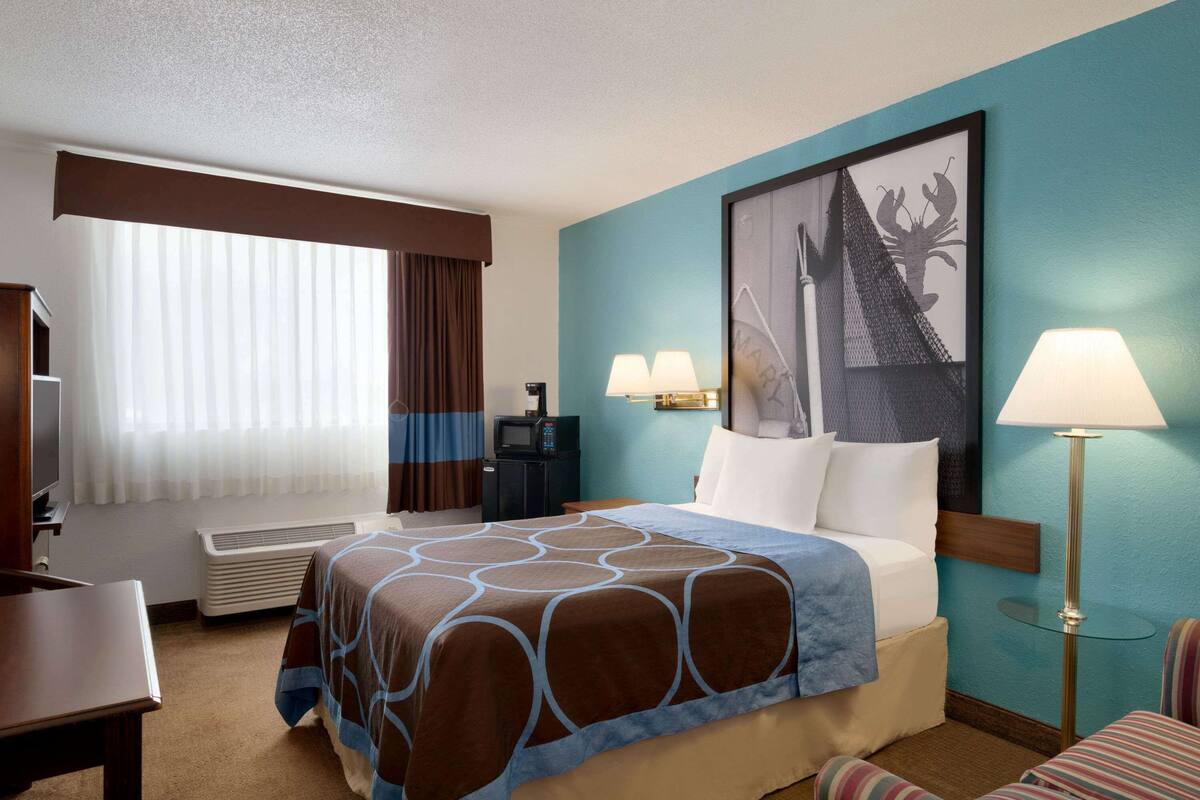 A hotel room with a bed, a desk, a chair, a TV, and a window with curtains.
