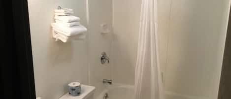 A bathroom with a bathtub, toilet, and sink. There are towels stacked on a shelf and a roll of toilet paper on the counter.