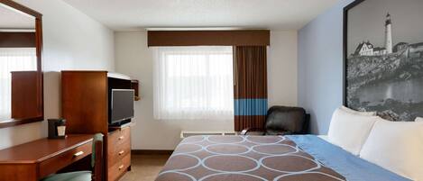 A hotel room with a bed, a desk, a chair, a television, and a painting of a lighthouse.