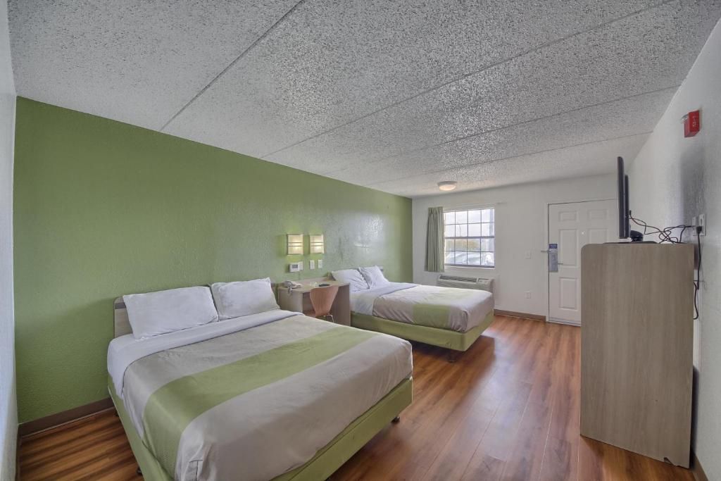 Quarto de hotel com duas camas, uma escrivaninha, uma cadeira, um guarda-roupa e uma janela.