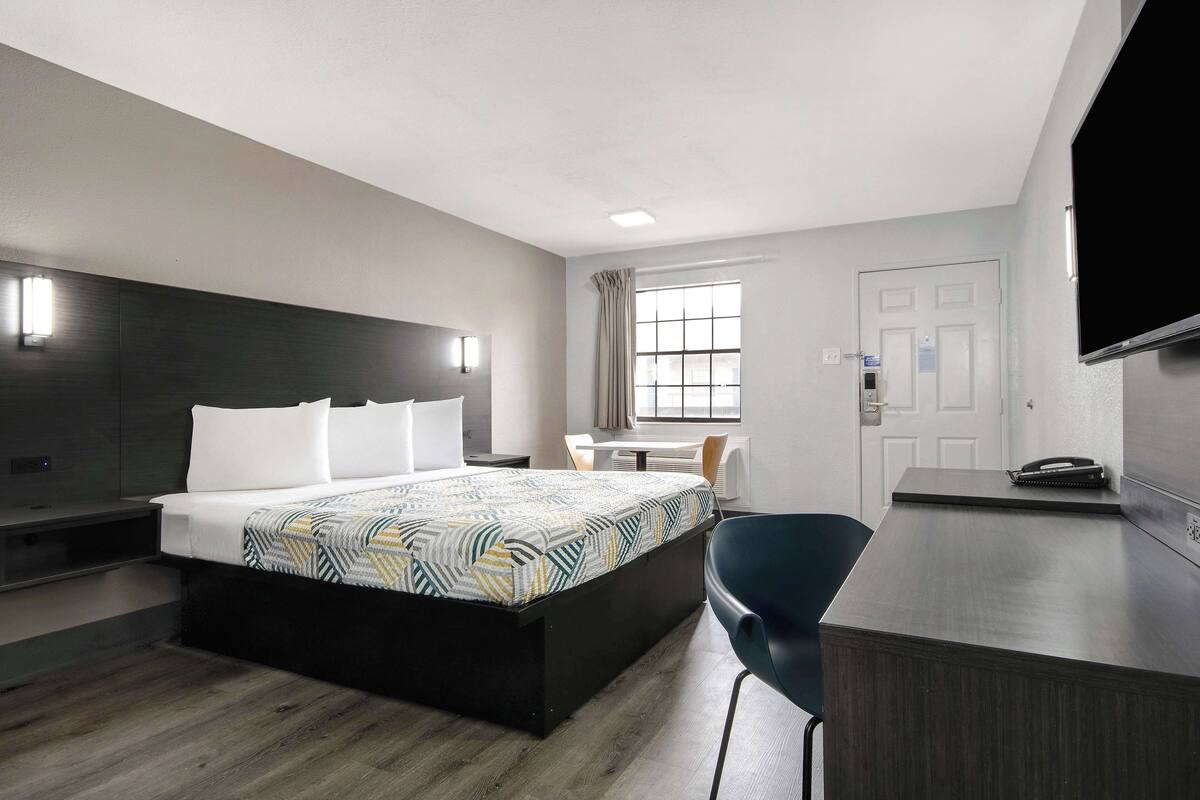 Une chambre d’hôtel équipée d’un lit, d’un bureau, d’une chaise, d’une télévision et d’une fenêtre avec des rideaux.
