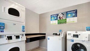 A laundry facility with multiple washing machines, a drying rack, and instructional posters on the wall.