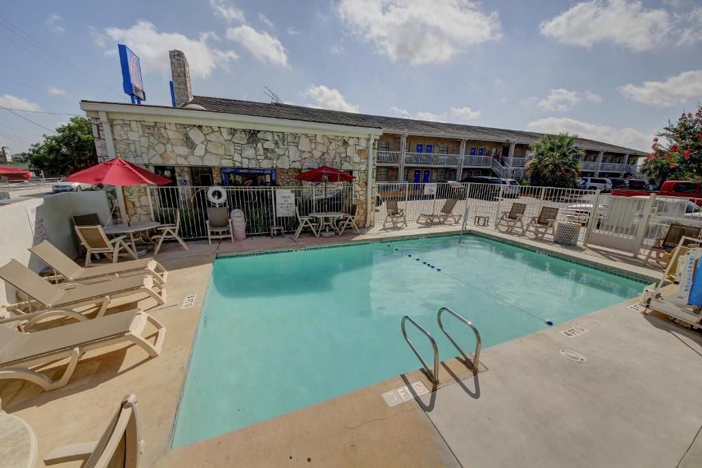 A swimming pool with lounge chairs and umbrellas, a stone building with a balcony, and a parking area.
