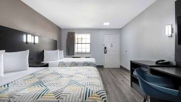 A hotel room with two beds, a desk, a chair, a TV, and a window with curtains.