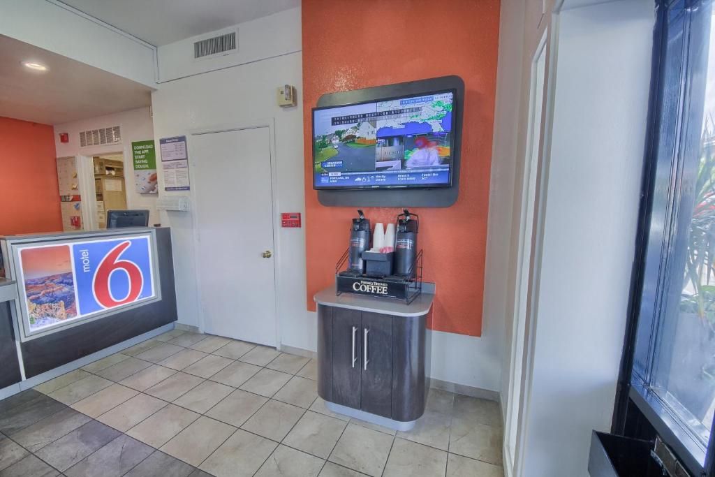 A hotel lobby with a reception desk, a digital screen displaying information, and a coffee station.