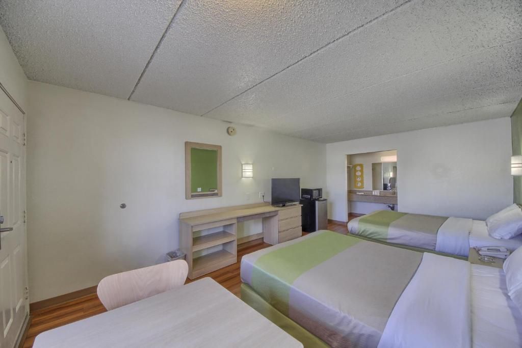 A hotel room with two beds, a desk, a television, and a mirror.