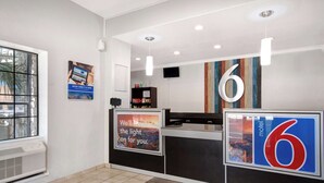 A hotel reception area with a large number '6' sign, a poster advertising direct booking, and a view of the outside through a window.