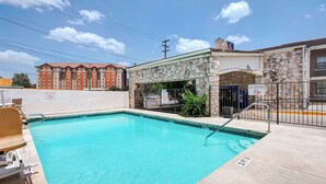 A swimming pool with a stone wall and a 'No Diving' sign, surrounded by a fence and a building with a stone facade.