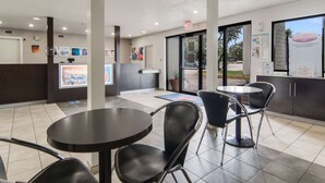 A clean, modern coffee shop interior with tables and chairs, a reception area, and a view of the outside.