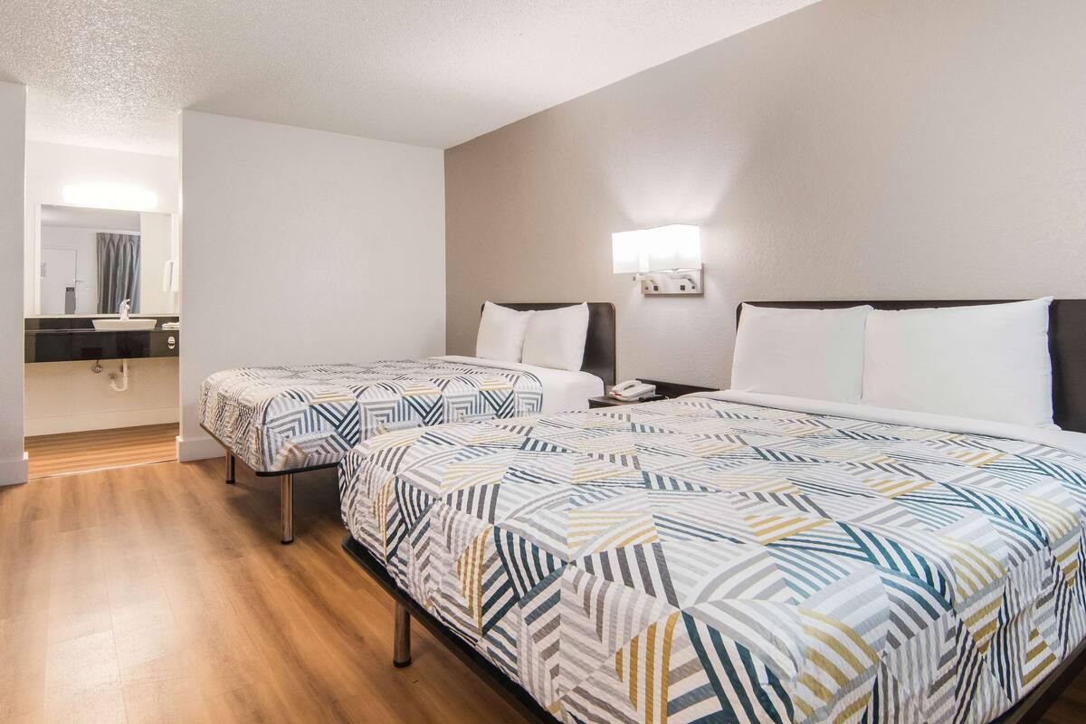 A hotel room with two beds, a bathroom, and a small desk.