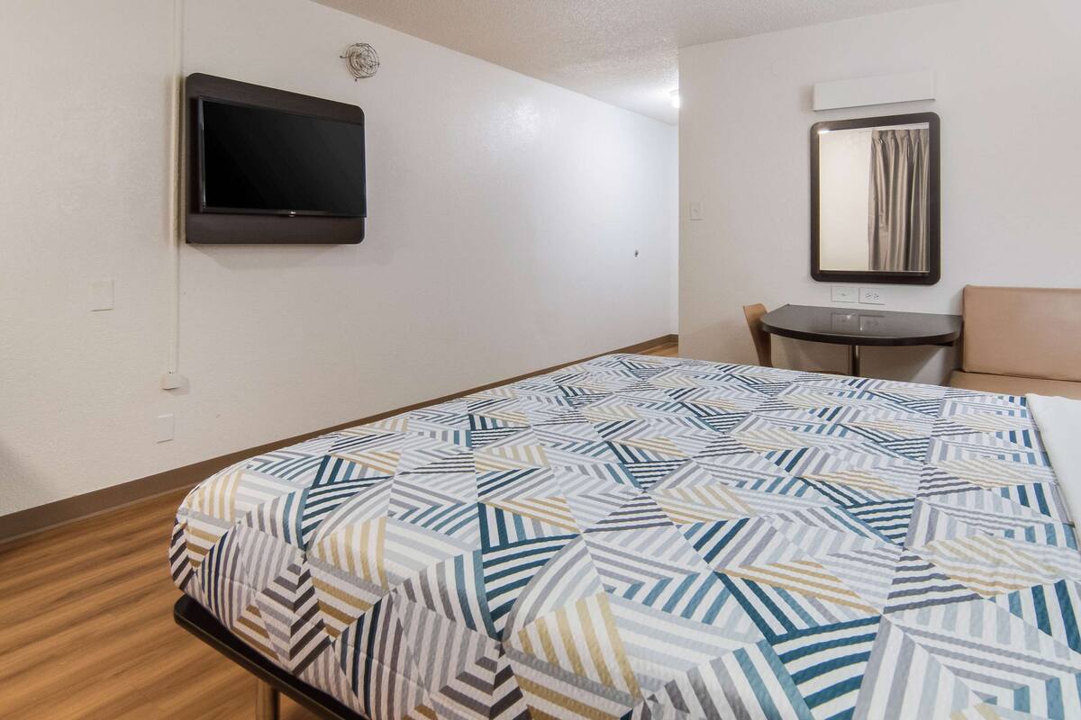 A hotel room with a bed, a TV mounted on the wall, a small table, and a chair.