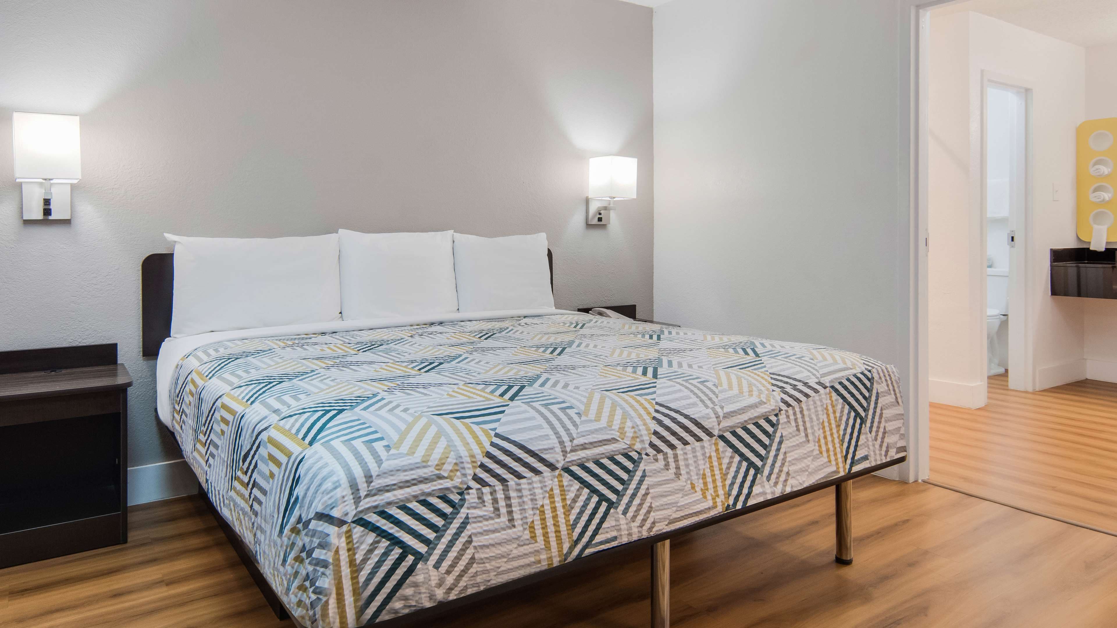 A neatly made bed with a patterned bedspread, two wall-mounted lamps, and a wooden floor.