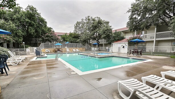 A swimming pool with lounge chairs and umbrellas, surrounded by a fence and trees.