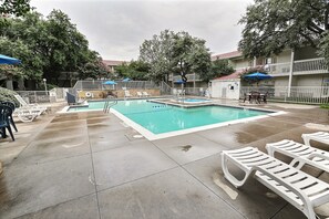 A swimming pool with lounge chairs and umbrellas, surrounded by a fence and trees. - Motel 6 Addison, TX - Dallas (Addison)