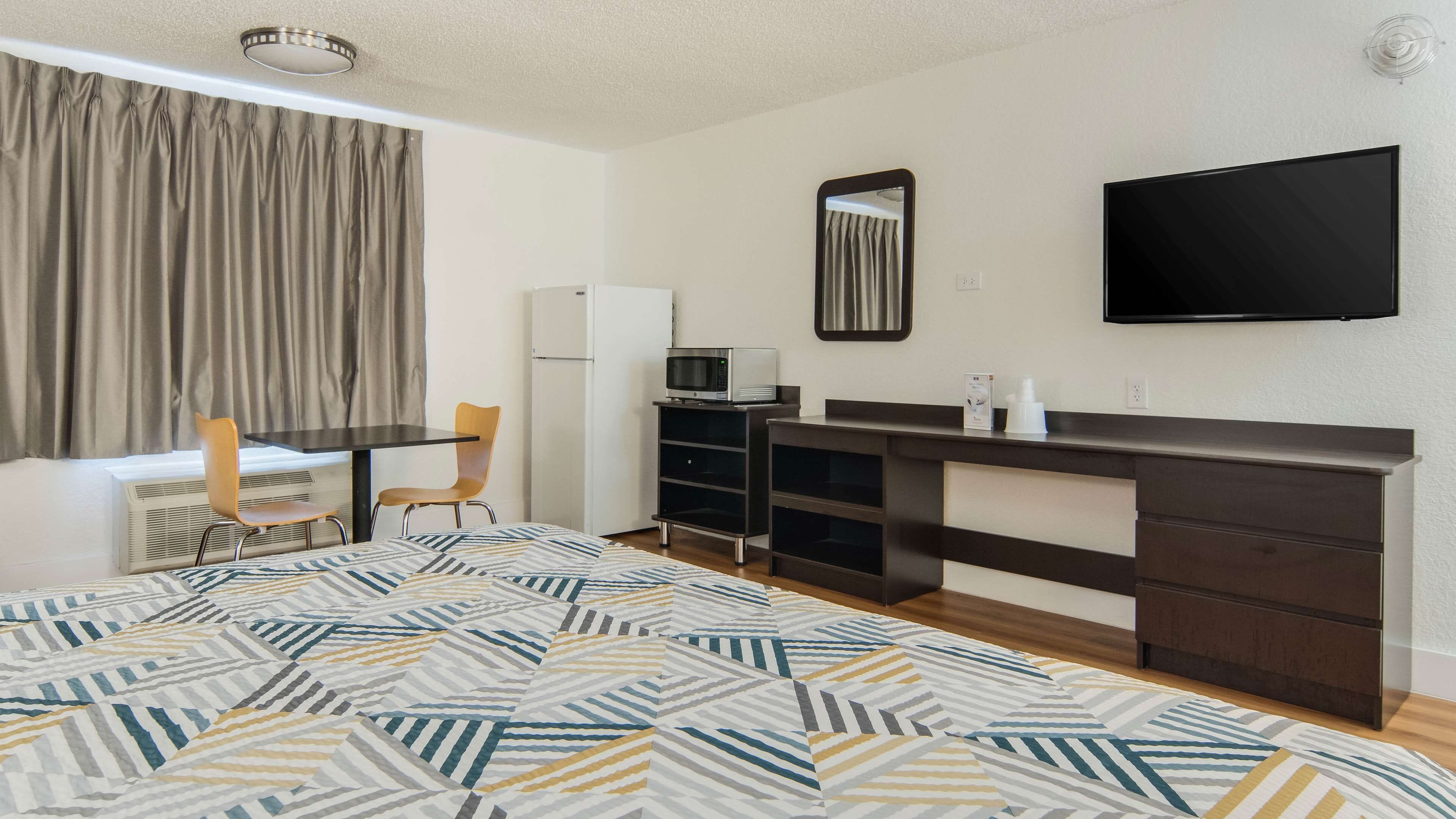 Habitación de hotel pequeña con cama, escritorio con silla, televisor, microondas y refrigerador.