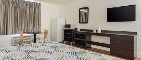 Habitación de hotel pequeña con cama, escritorio con silla, televisor, microondas y refrigerador.