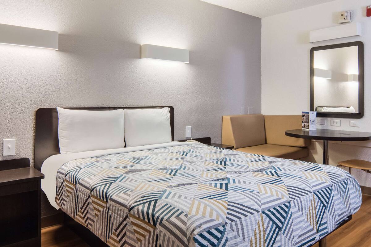 A hotel room with a bed, a desk, a chair, and a mirror.