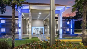 A hotel entrance with a 'welcome' sign, a covered walkway, and a landscaped garden.