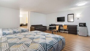 A hotel room with a bed, two chairs, a desk, a television, and a refrigerator.