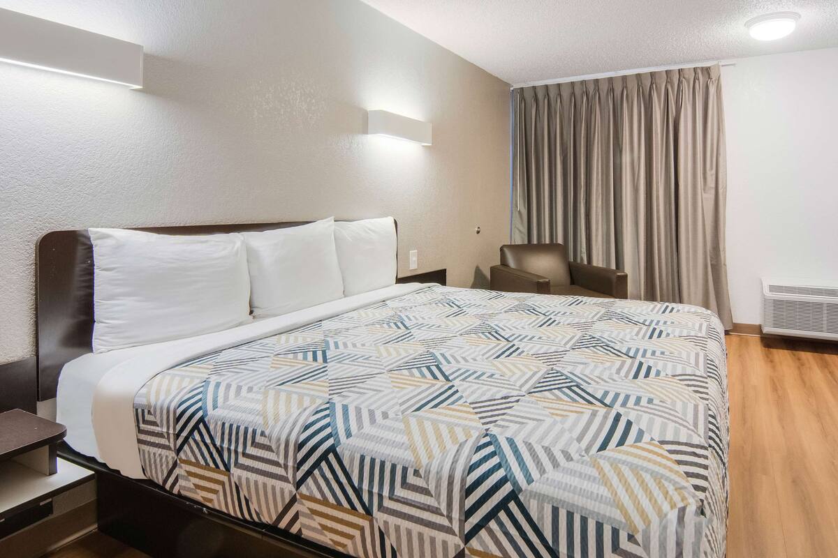A hotel room with a large bed, a desk, a chair, a television, and a heater.