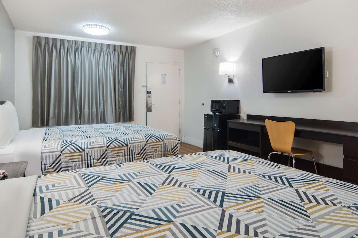 A hotel room with two beds, a TV, a desk, and a chair.