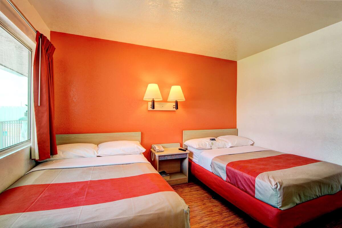A hotel room with two beds, a nightstand, and a window with curtains.