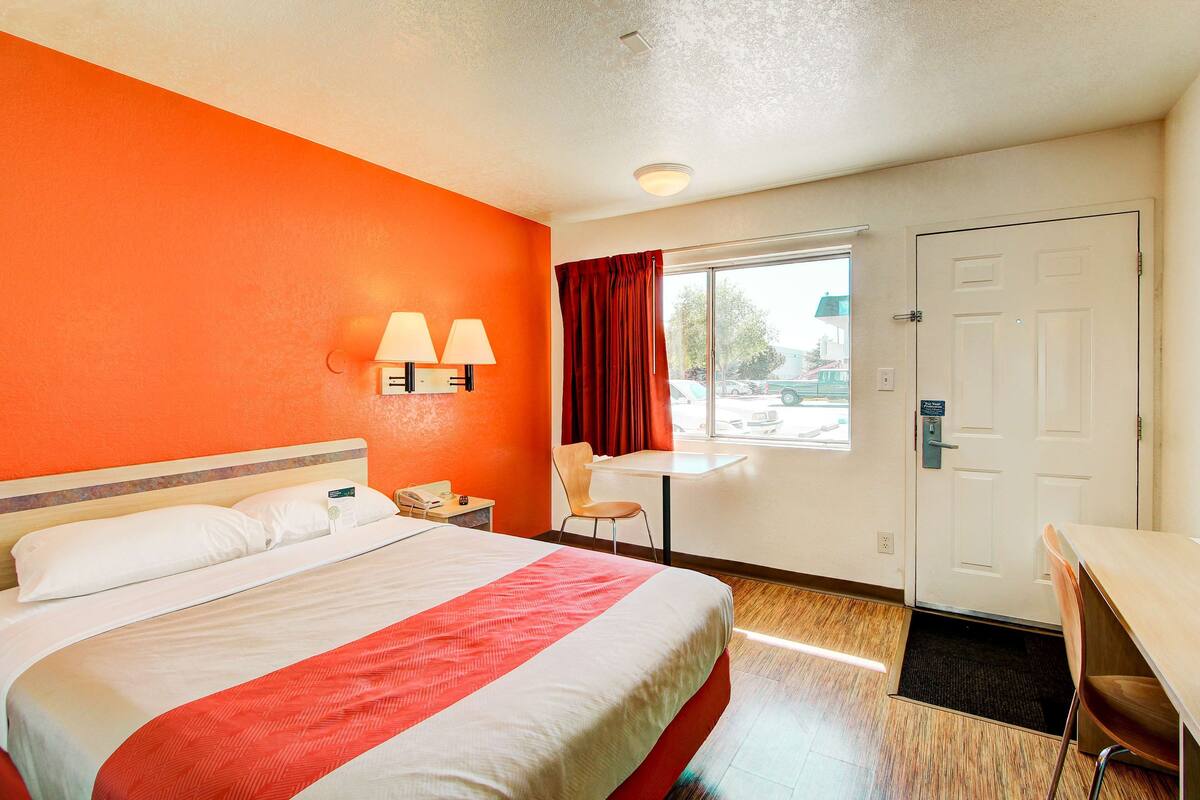 A hotel room with a bed, a desk, a chair, a window, and a door.
