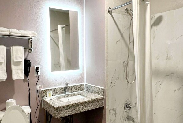 Een badkamer met een wastafel van graniet, een spiegel, een handdoekrek, een douche en een toilet.