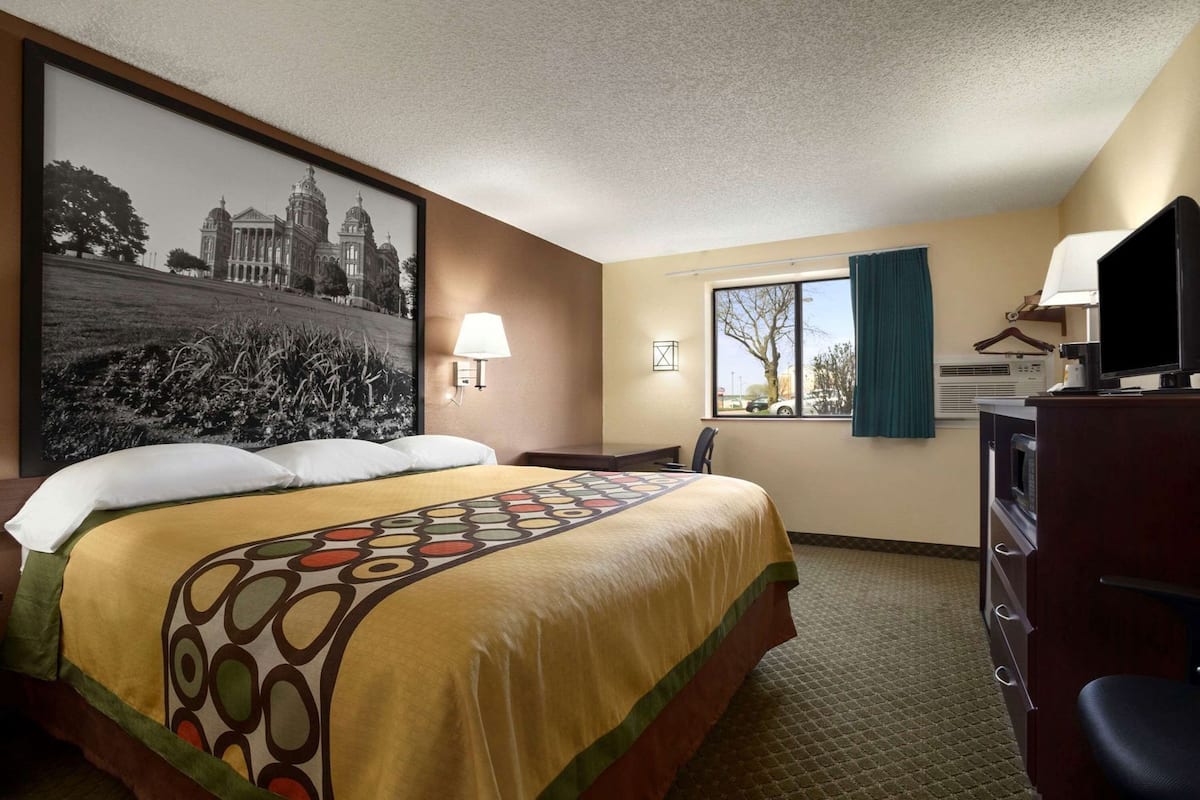 Una habitación de hotel con cama, escritorio, televisor y ventana con cortinas.