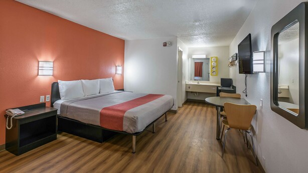 Una habitación de hotel con cama, mesita de noche, silla, escritorio y espejo.
