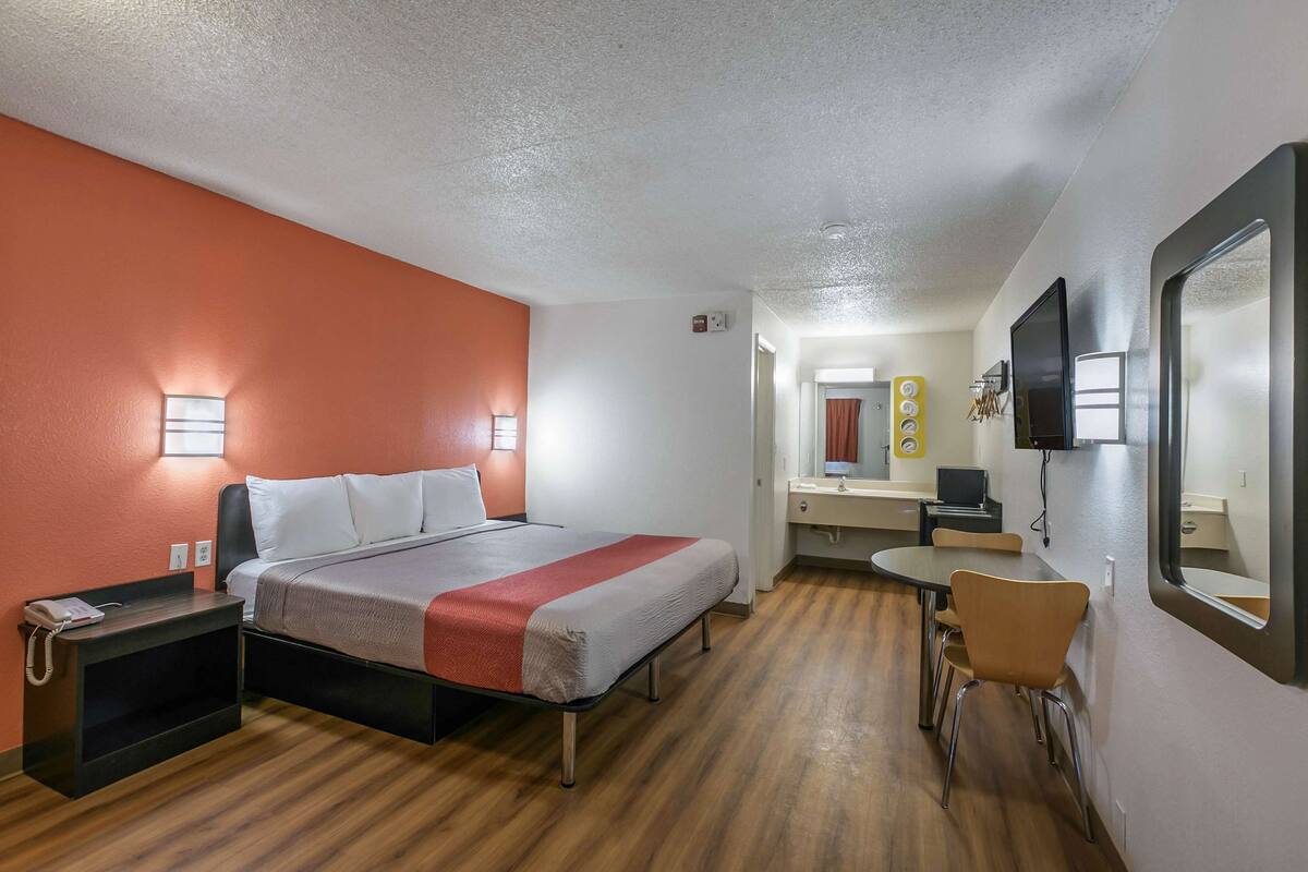A hotel room with a bed, bedside table, chair, desk, and a mirror.
